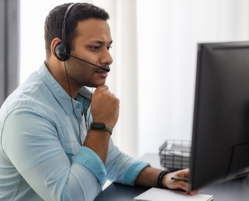 Concentrated man call center worker in headphones is working at modern office. Portrait of Asian male support employee